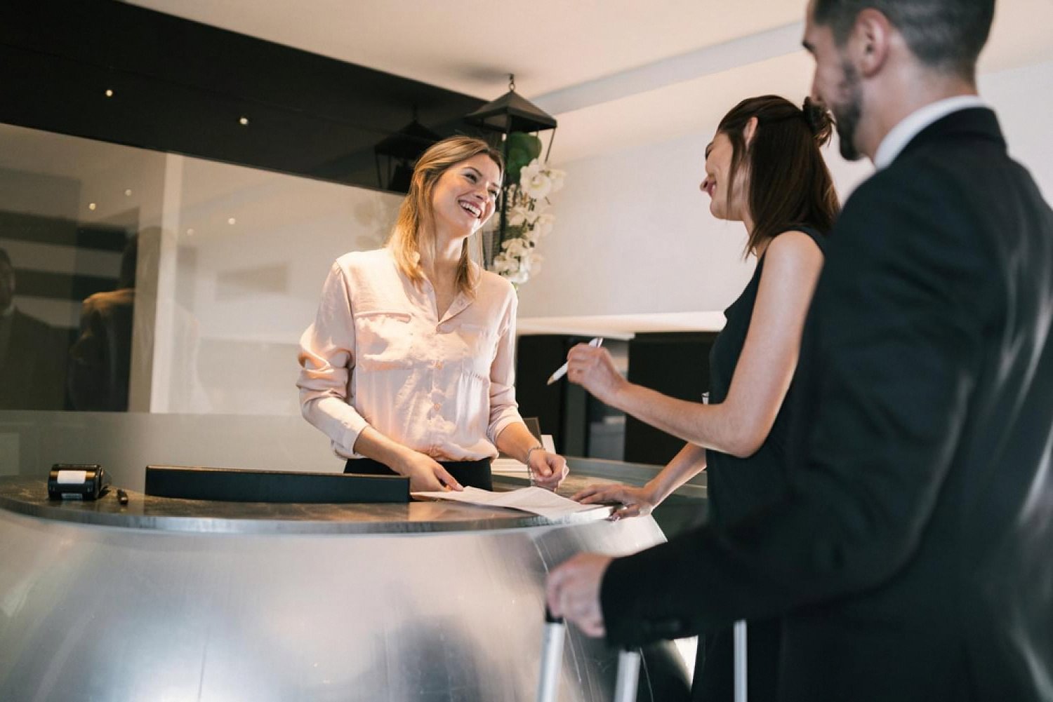 Hotel receptionist smiling while assisting two guests with mobile check-in