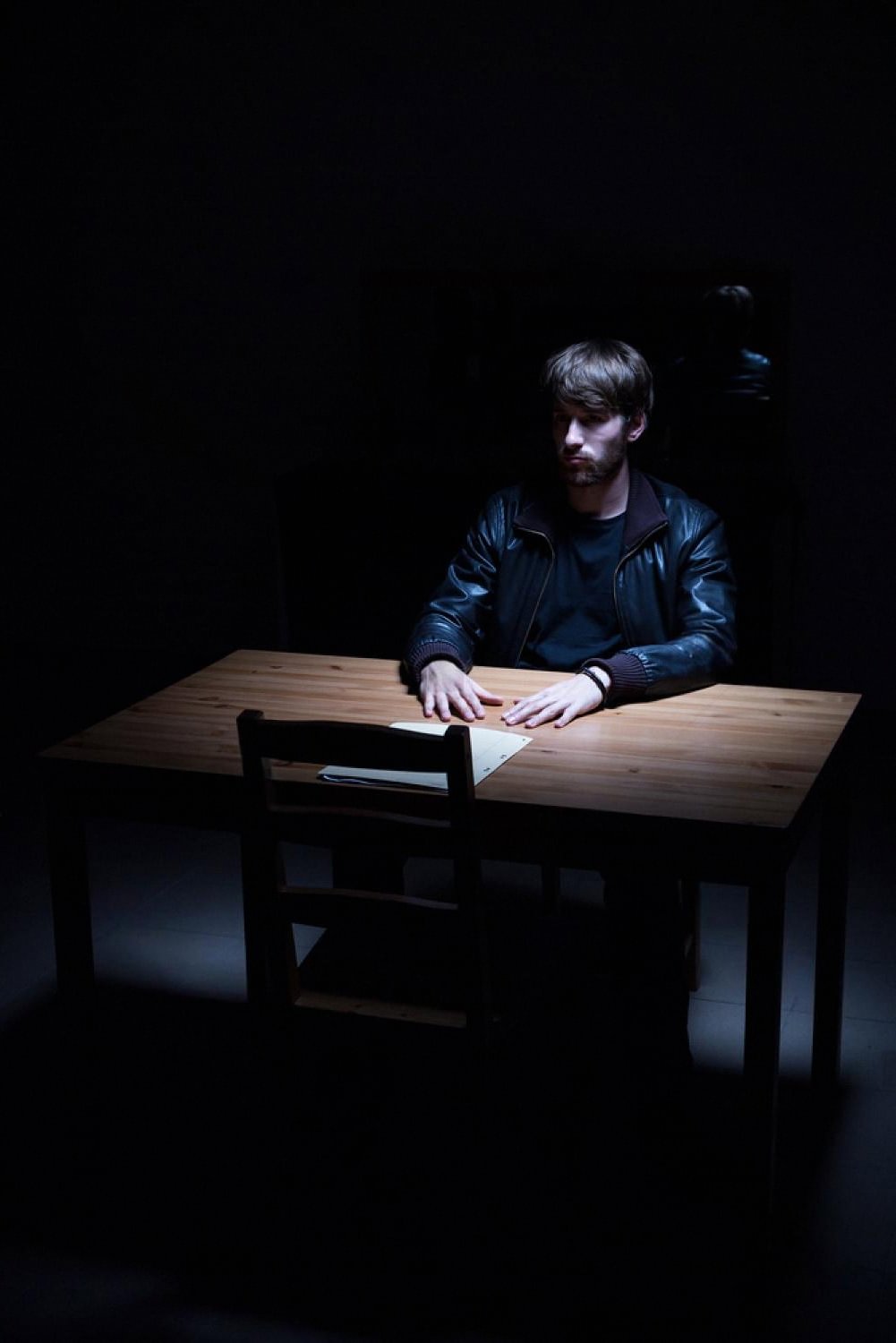Man sitting alone under a spotlight in a dark interrogation room, representing a criminal case in the UAE