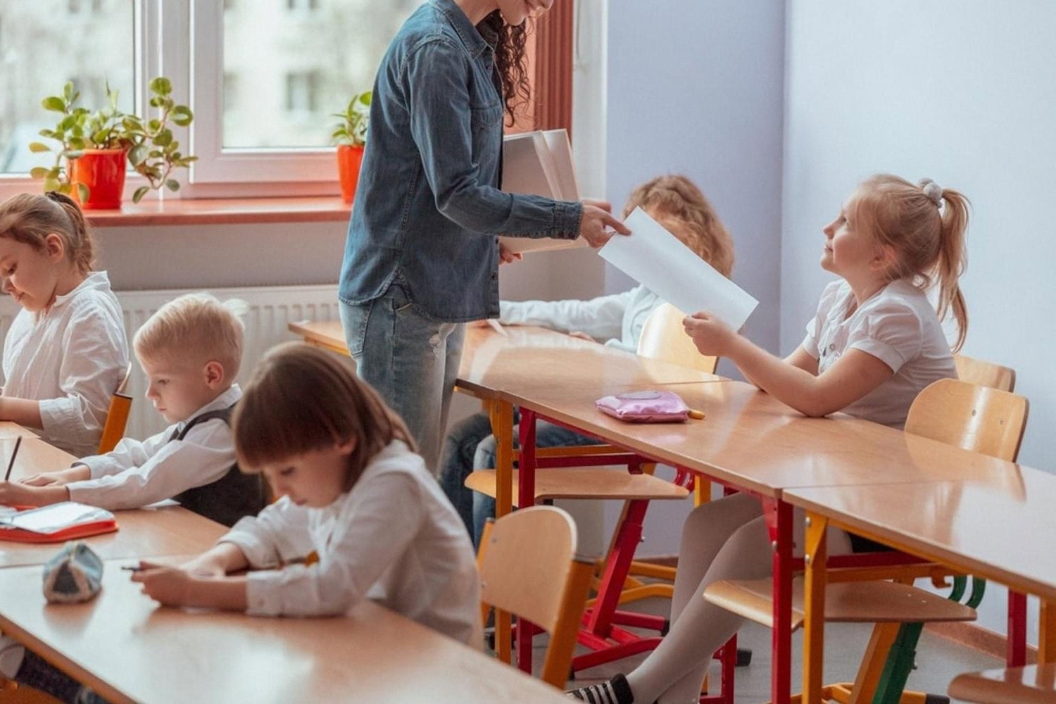 Teacher handing out papers to young pupils working in a classroom